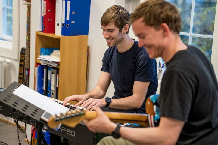To instruktører som ler sammen og spiller hvert sitt instrument