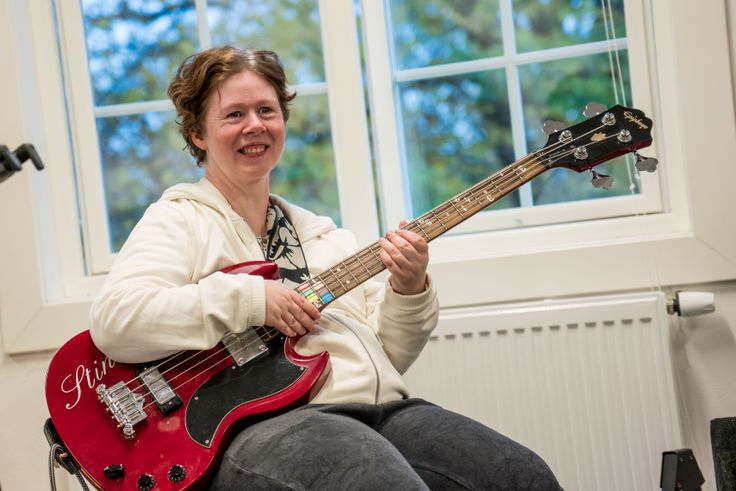 Dame som smiler med gitar som har fargetonatsjon på halsen, i klasserom 