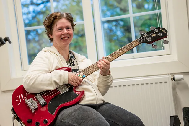 Dame som smiler med gitar som har fargetonatsjon på halsen, i klasserom 
