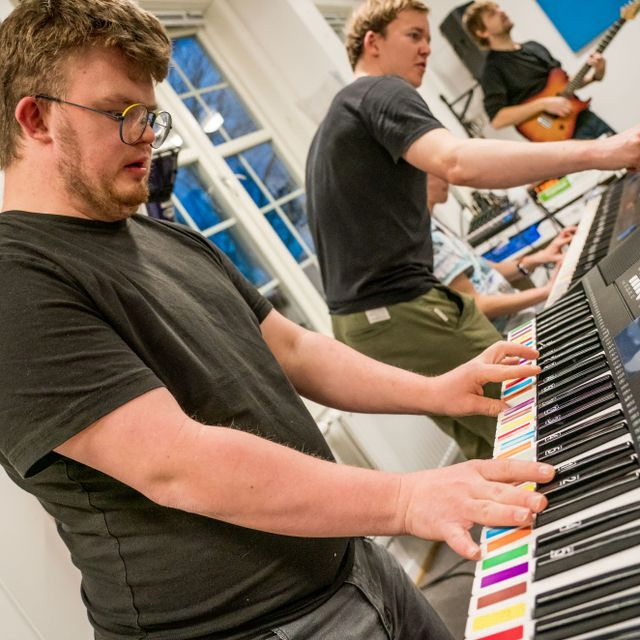 Musiker på keyboard og instruktører i bakgrunnen