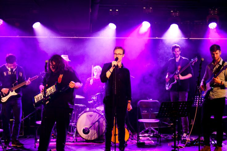 Band med 6 medlemmer på scenen med lilla lys